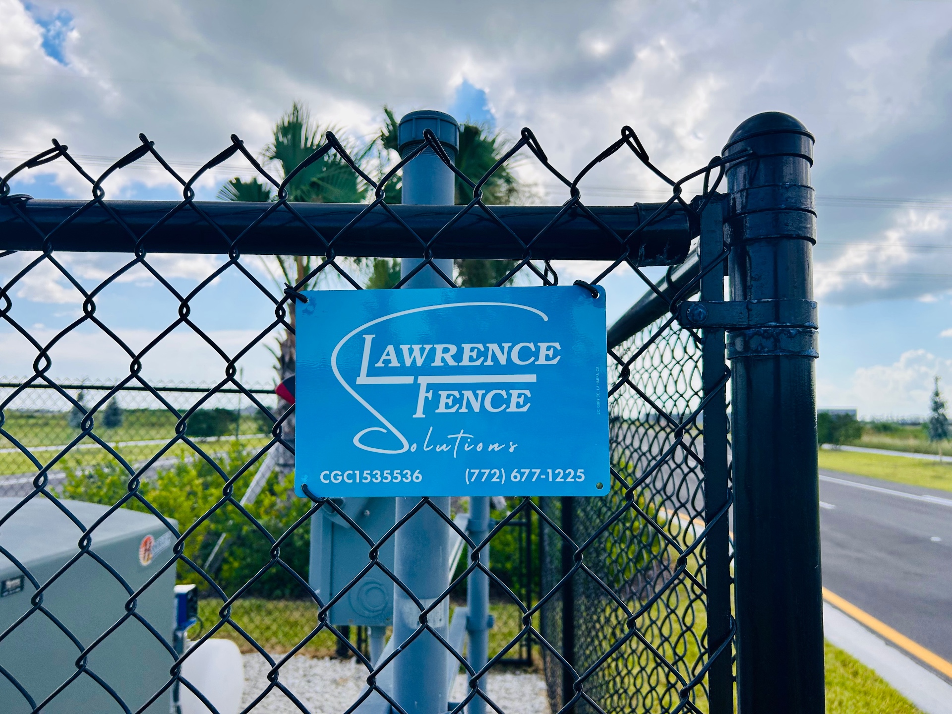 Lawrence Fence Solutions sign on black chain-link commercial gate in Martin County, FL