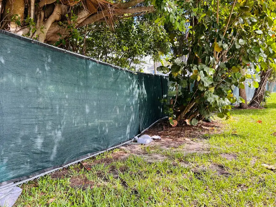 Temporary fence panels with green privacy screen installed around mature trees