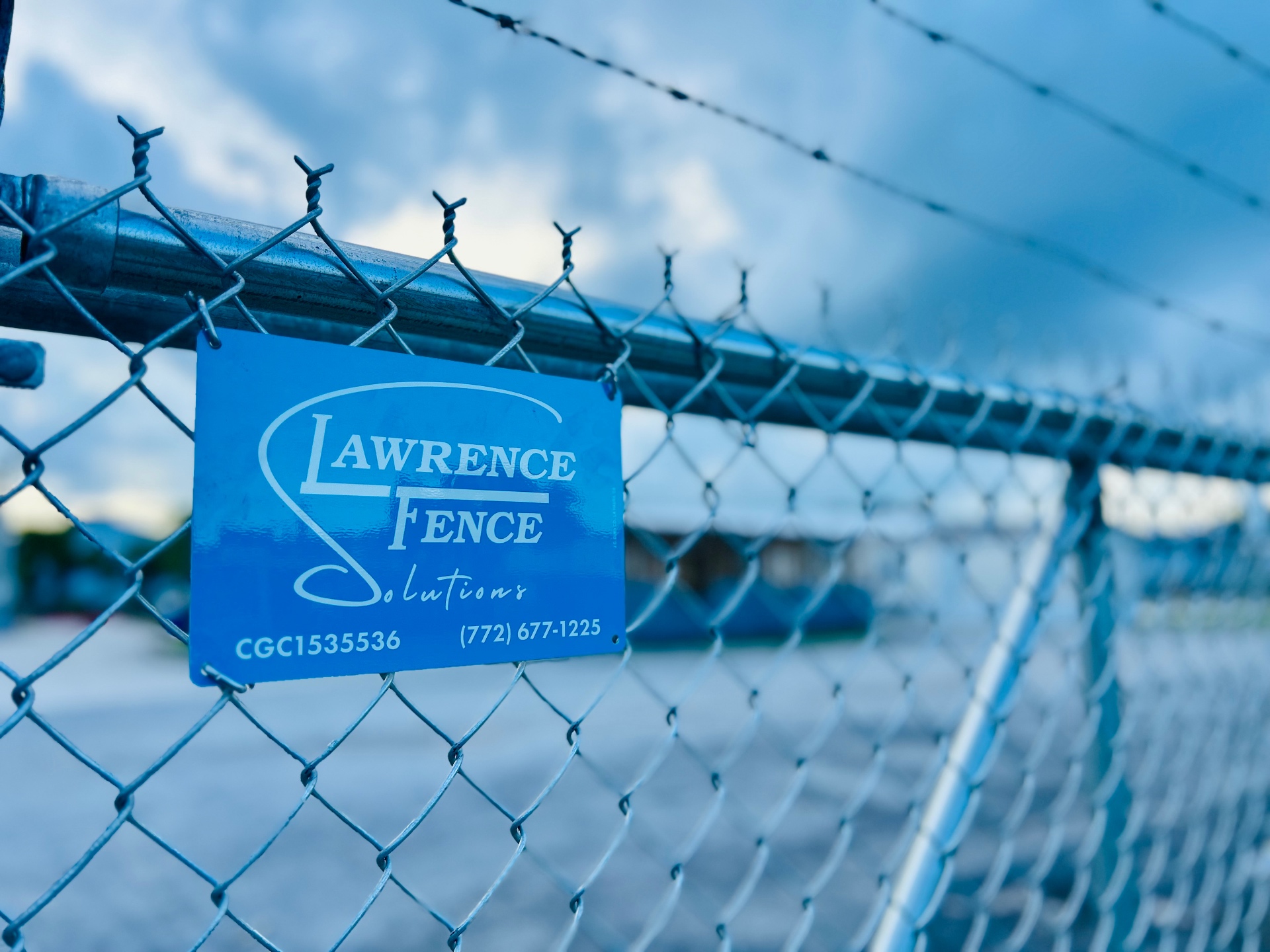 Lawrence Fence Solutions sign on galvanized chain-link commercial perimeter in St. Lucie County, FL
