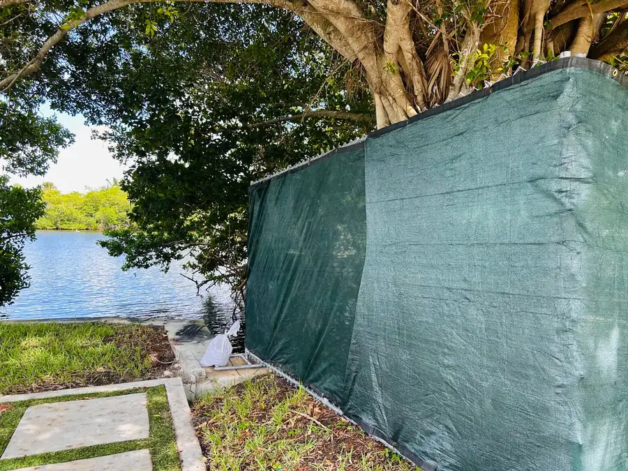 Free-standing temporary fence panels with green privacy screen beside a Florida waterfront