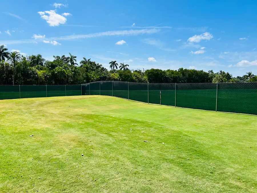 Post-driven chain-link fence with green windscreen surrounding a landscaped Florida property