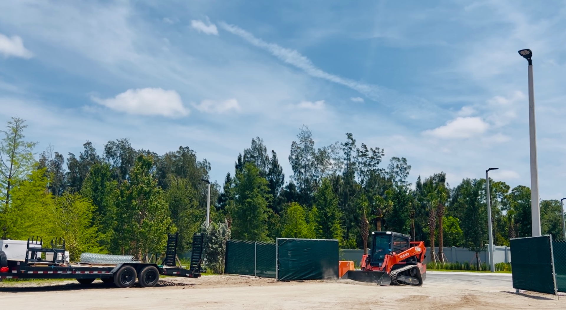 Temporary chain-link fence with green privacy screen and access opening at an active Florida job site