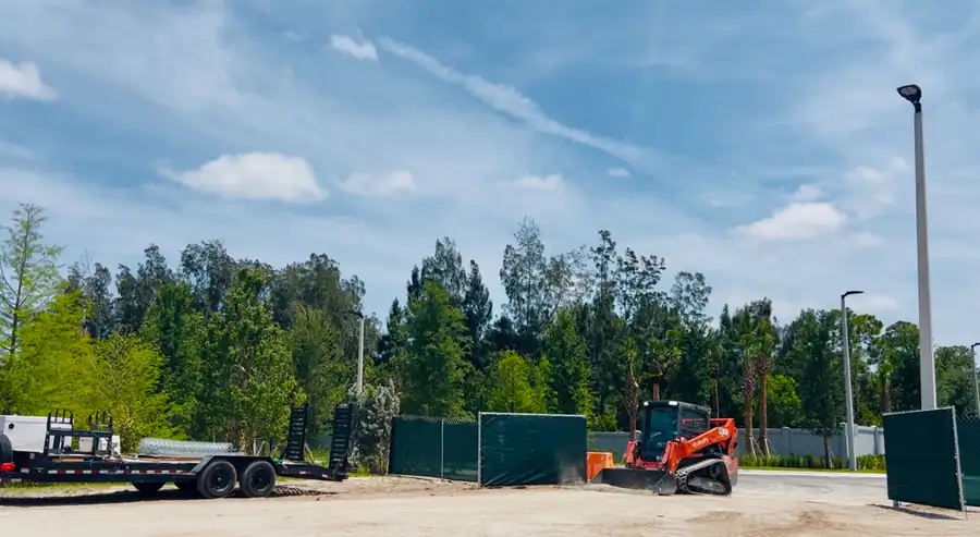 Temporary chain-link fence with green privacy screen and access opening at an active Florida job site